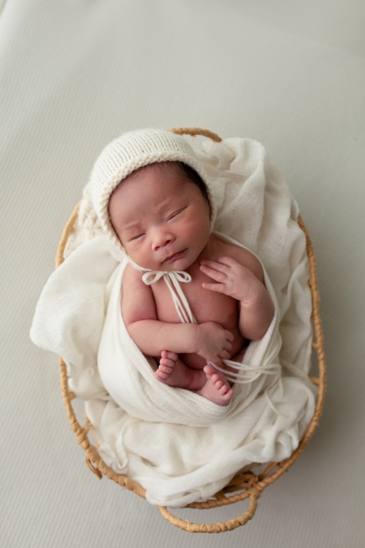 Newborn in a cream knit bonnet resting in a basket