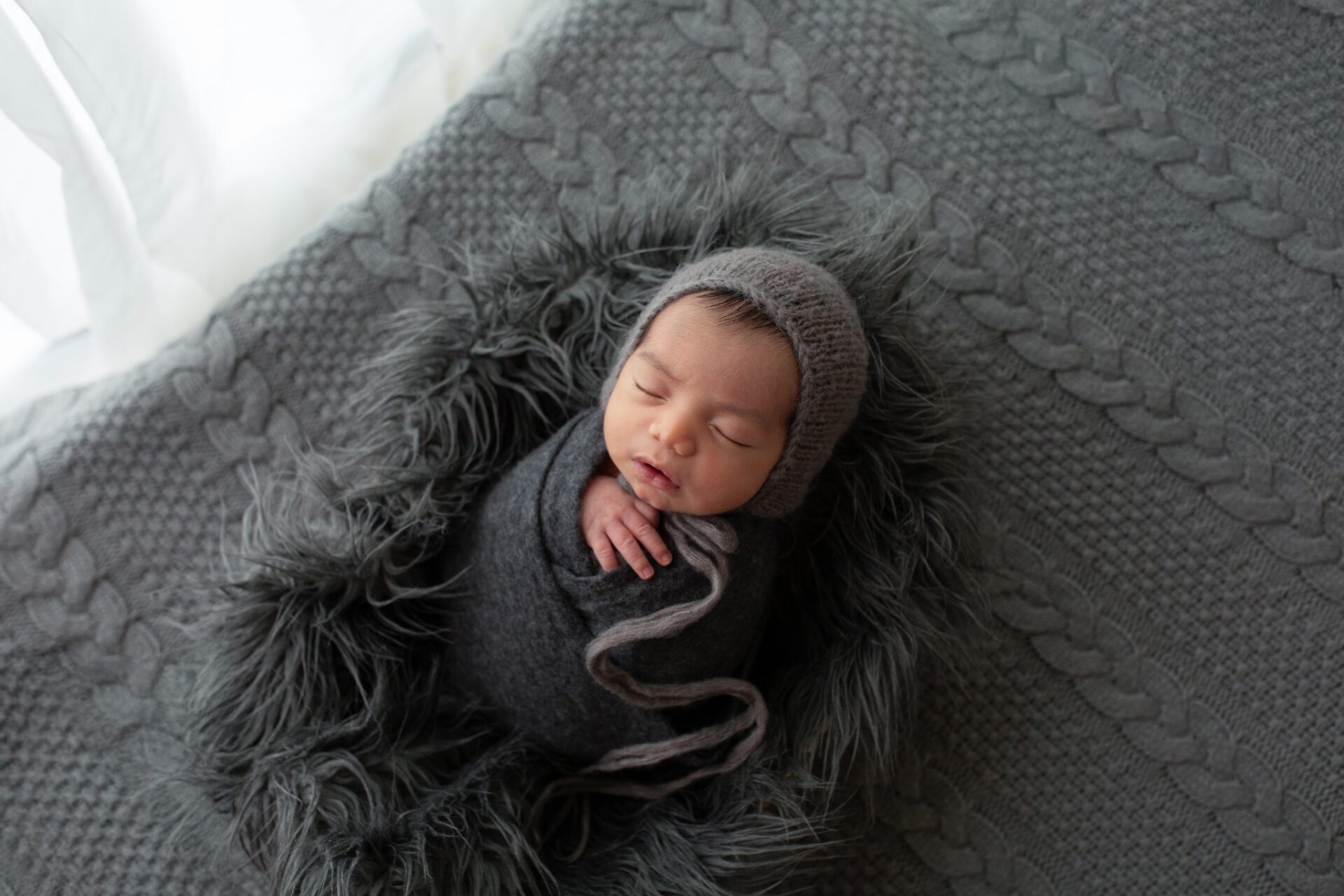 Sleeping newborn wrapped in charcoal with a knit bonnet