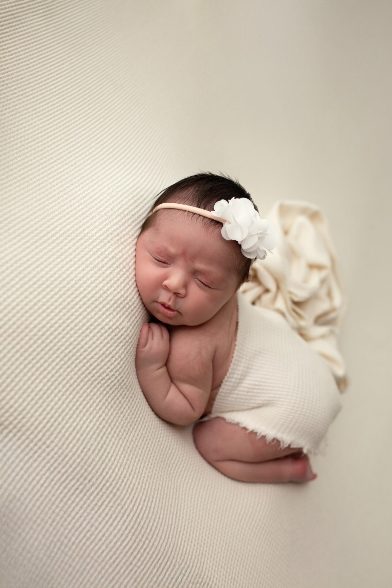 Newborn resting on a cream blanket with a white floral headband