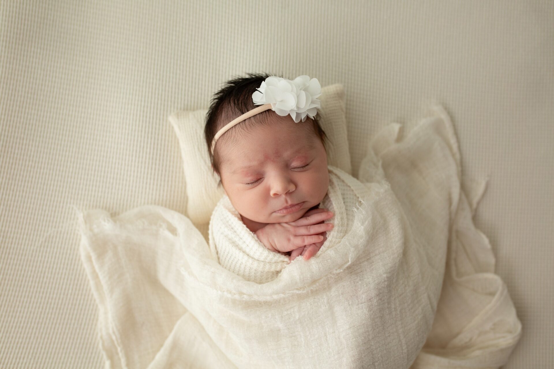 Swaddled newborn with hands tucked beneath their chin
