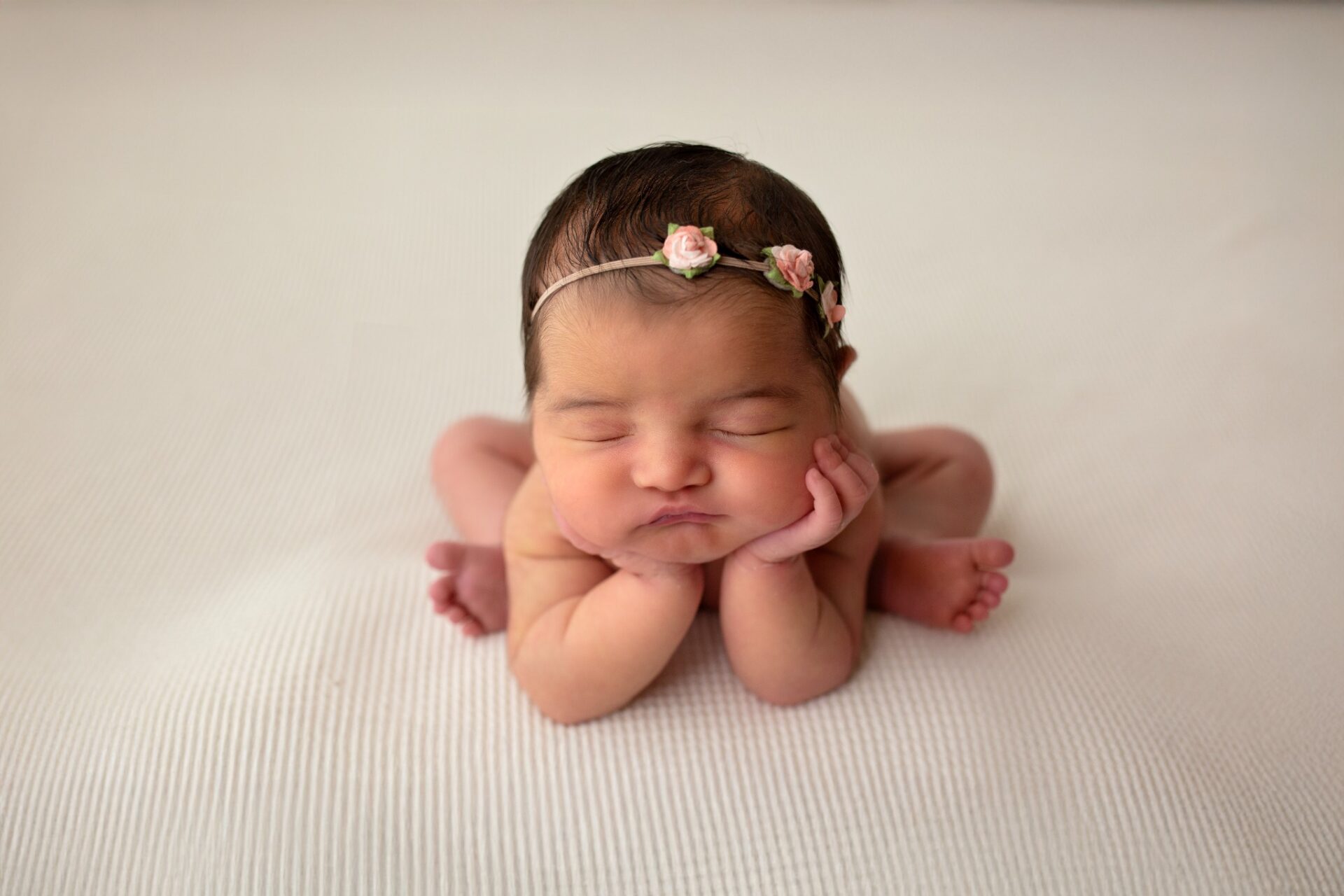 Sleeping newborn with a pink floral headband on a cream blanket