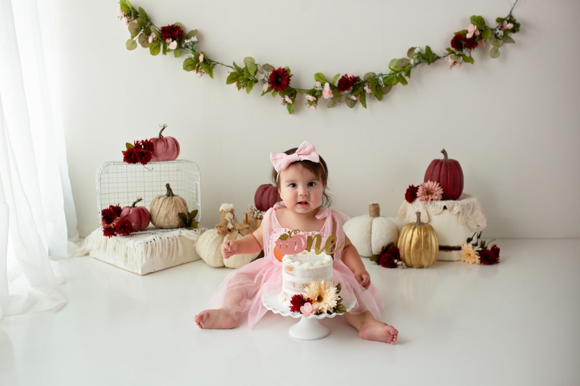 Baby with a first birthday cake and pink pumpkin decorations