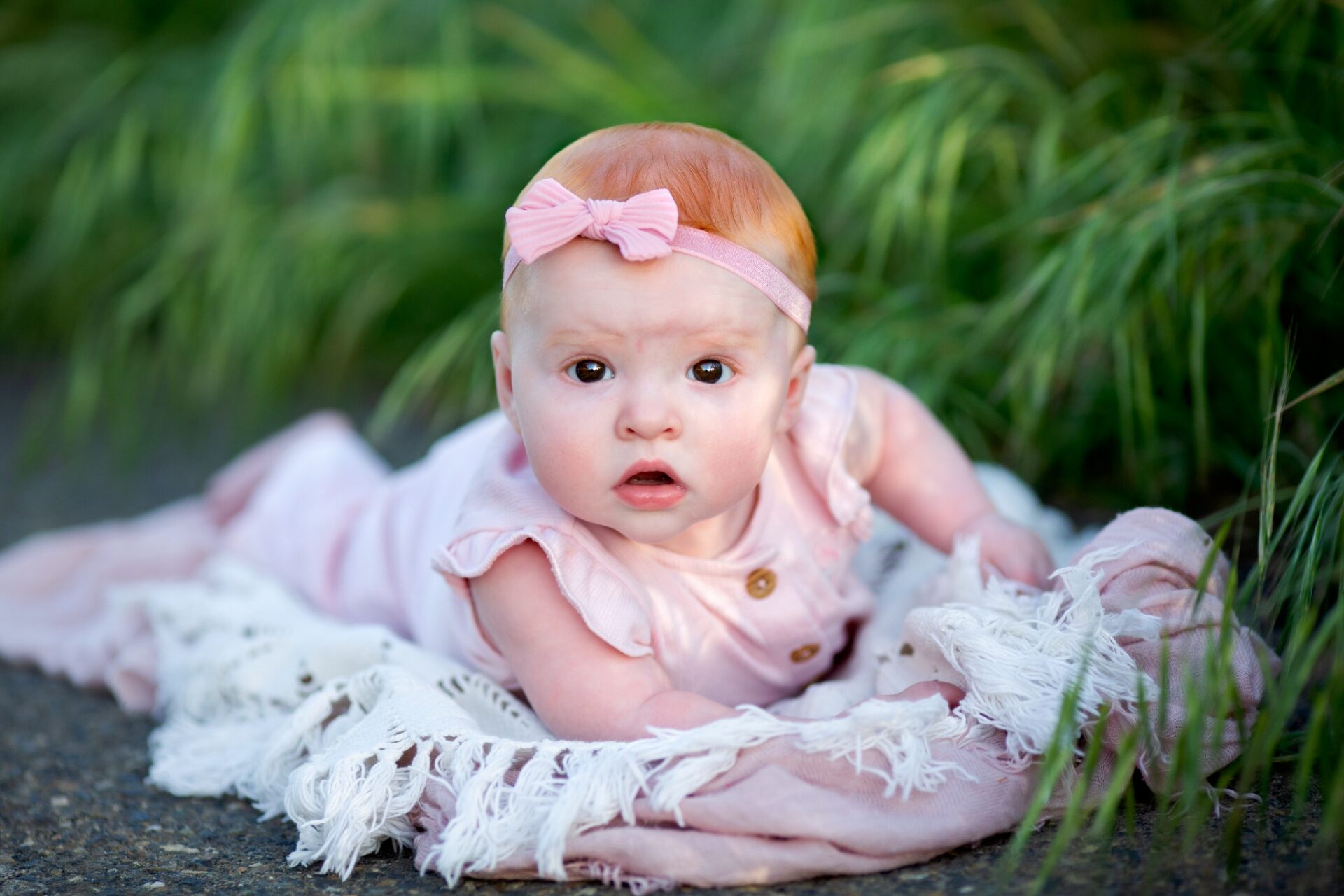 Baby girl with a pink bow enjoying tummy time on a blanket outdoors