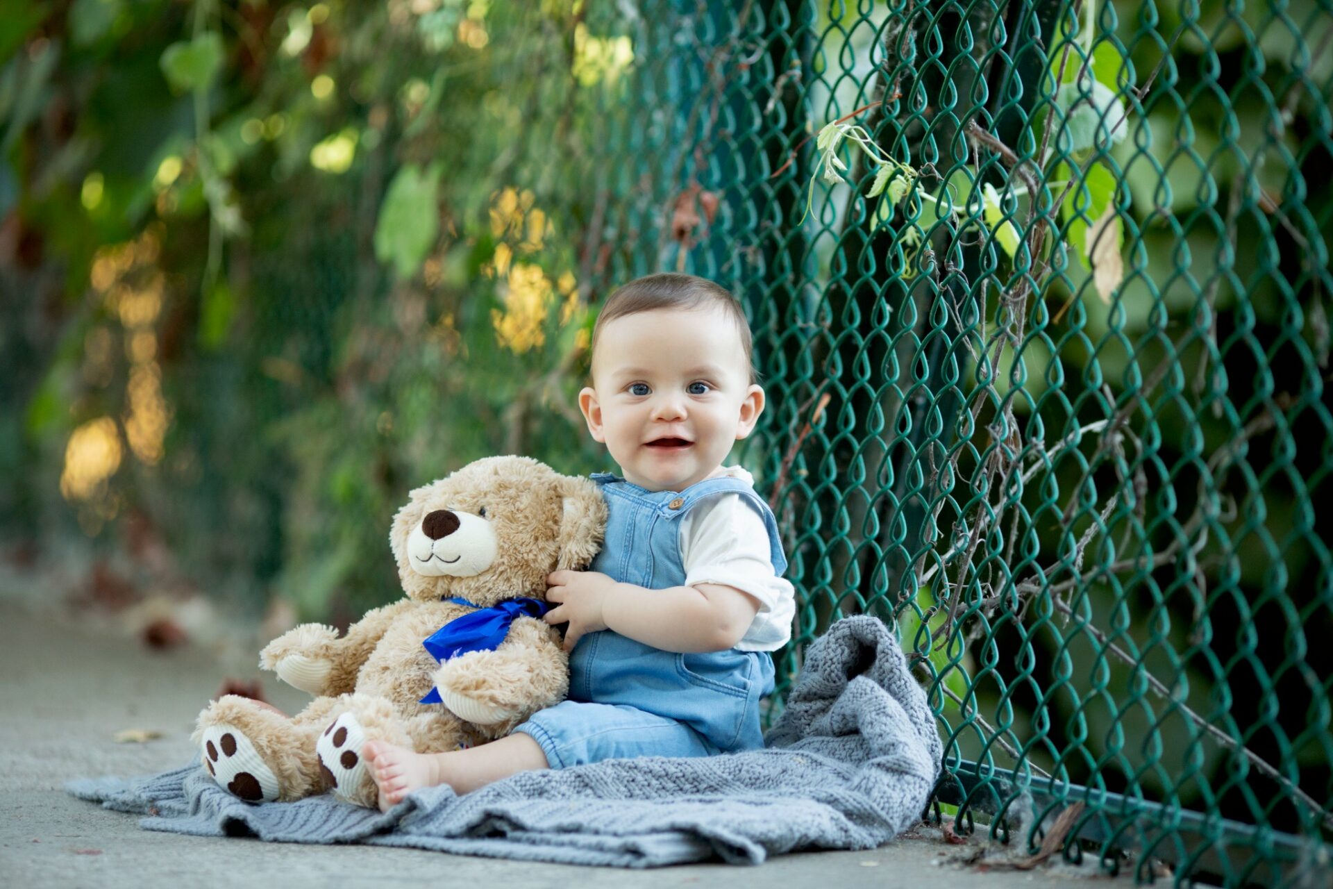 Sitting baby holding a teddy bear during an outdoor milestone portrait session