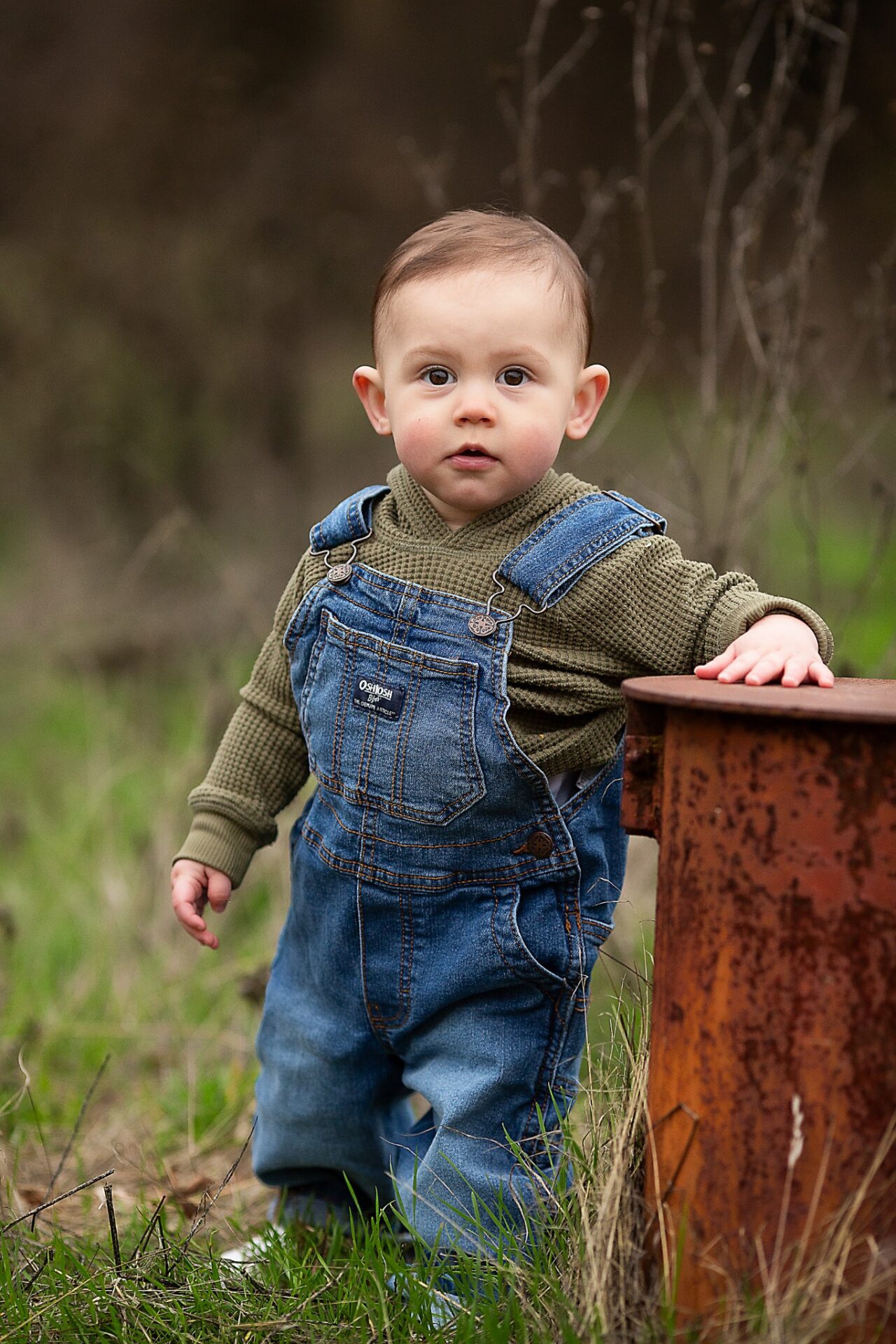 Baby boy standing with support beside a wooden box outdoors