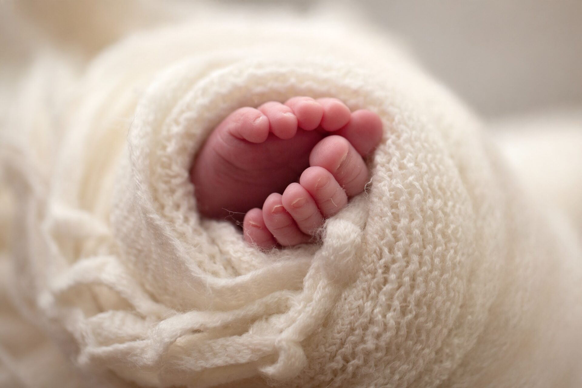Tiny newborn toes tucked into a soft cream wrap